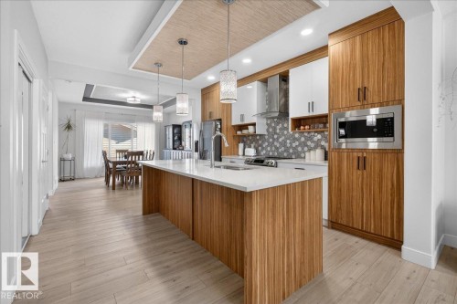 This kitchen features modern cabinetry with integrated stainless steel appliances, a spacious island with a white countertop, and contemporary pendant lighting - 1778 25A Street, Edmonton, AB - Indoor Photo Showing Kitchen With Upgraded Kitchen