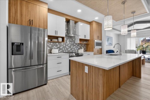 The kitchen features a large island with a white countertop and wood paneling, a stainless steel refrigerator, and wood and white cabinetry - 1778 25A Street, Edmonton, AB - Indoor Photo Showing Kitchen With Upgraded Kitchen