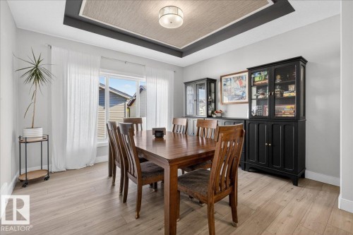 Dining area featuring light-toned flooring, a window providing natural light, and a tray ceiling with a central light fixture - 1778 25A Street, Edmonton, AB - Indoor Photo Showing Dining Room