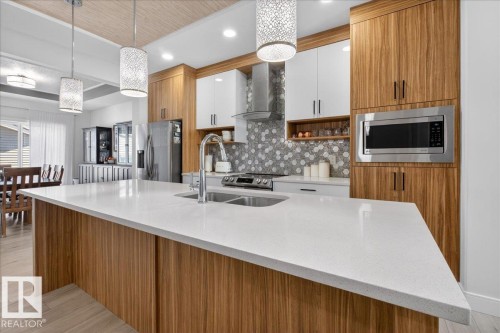 Modern kitchen featuring a large island with a light-colored countertop, wooden cabinetry, stainless steel appliances, and a tiled backsplash - 1778 25A Street, Edmonton, AB - Indoor Photo Showing Kitchen With Double Sink With Upgraded Kitchen