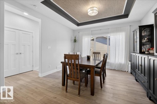 Dining area featuring light-toned flooring, a window with sheer curtains, and a tray ceiling with a central light fixture - 1778 25A Street, Edmonton, AB - Indoor Photo Showing Dining Room