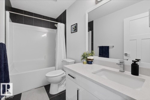 Bathroom featuring a white bathtub and shower with dark tiled walls, a white vanity with a light-colored countertop and integrated sink, and a large mirror - 1778 25A Street, Edmonton, AB - Indoor Photo Showing Bathroom