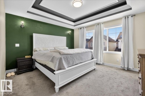 This room features a tray ceiling with recessed lighting, wall sconces, and neutral carpet flooring - 1778 25A Street, Edmonton, AB - Indoor Photo Showing Bedroom