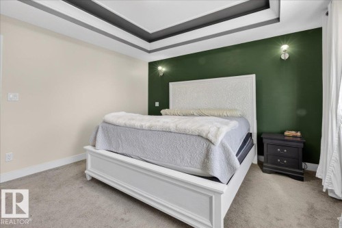 The bedroom features a tray ceiling with dark and light accents, light-colored carpeting, and a contrasting dark green accent wall with wall-mounted light fixtures - 1778 25A Street, Edmonton, AB - Indoor Photo Showing Bedroom