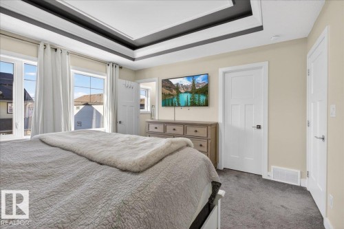 This room features a tray ceiling with dark accents, multiple windows providing natural light, and plush grey carpeting - 1778 25A Street, Edmonton, AB - Indoor Photo Showing Bedroom
