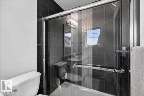 The bathroom features a glass-enclosed shower with dark tile surround, accented by a section of lighter-toned subway tile - 1778 25A Street, Edmonton, AB - Indoor Photo Showing Bathroom