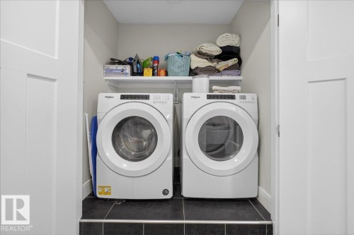 Dedicated laundry area featuring a white front-loading washer and dryer, dark tiled flooring, and a white storage shelf - 1778 25A Street, Edmonton, AB - Indoor Photo Showing Laundry Room