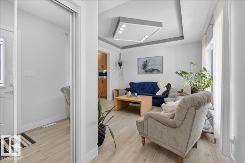 The living space features light-toned flooring, a tray ceiling with integrated lighting, and a large window with sheer curtains - 1778 25A Street, Edmonton, AB - Indoor