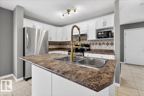 Kitchen featuring stainless steel appliances, white cabinetry, light tile patterned floors, a textured ceiling, and an island with sink - 150 Acacia Circle, Leduc, AB - Indoor Photo Showing Kitchen With Double Sink