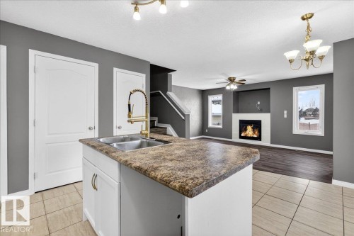 Kitchen with white cabinets, light tile patterned floors, a glass covered fireplace, hanging light fixtures, and a textured ceiling - 150 Acacia Circle, Leduc, AB - Indoor Photo Showing Kitchen With Fireplace With Double Sink