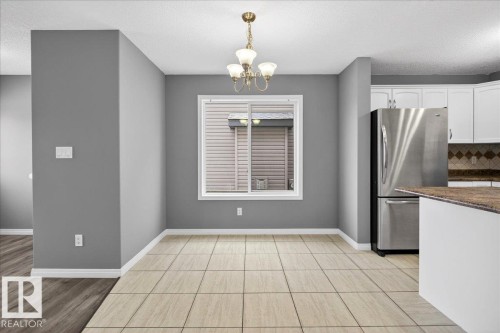 Kitchen with freestanding refrigerator, a chandelier, decorative backsplash, white cabinets, and a textured ceiling - 150 Acacia Circle, Leduc, AB - Indoor Photo Showing Kitchen