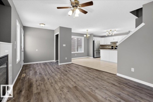 Unfurnished living room featuring light wood finished floors, a chandelier, a textured ceiling, and a ceiling fan - 150 Acacia Circle, Leduc, AB - Indoor Photo Showing Other Room With Fireplace
