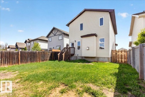 Rear exterior featuring light-colored siding, a wooden deck with stairs, a partial wooden privacy fence, and a wooden gate - 150 Acacia Circle, Leduc, AB - Outdoor