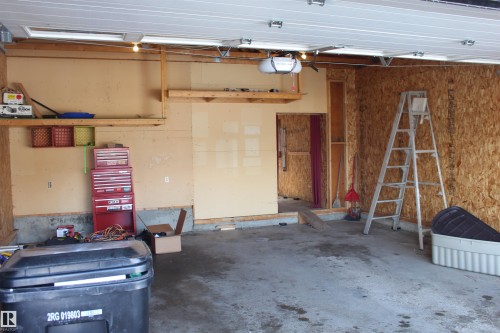The property features a garage with a concrete floor, exposed wood paneling on the walls, and overhead lighting - Edmonton, AB - Indoor Photo Showing Garage