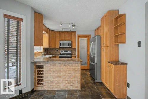 The kitchen features extensive wood cabinetry, a brick-textured island with integrated wine storage, and dark tile flooring - Edmonton, AB - Indoor Photo Showing Kitchen
