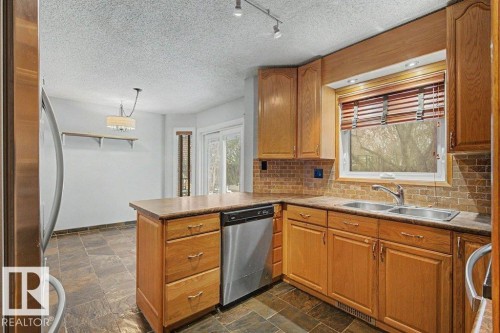 The kitchen features light wood cabinetry, a tiled backsplash, and stainless steel appliances - Edmonton, AB - Indoor Photo Showing Kitchen With Double Sink
