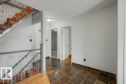 Entryway featuring a staircase with wooden treads and a decorative metal railing, alongside natural stone tile flooring - Edmonton, AB - Indoor Photo Showing Other Room