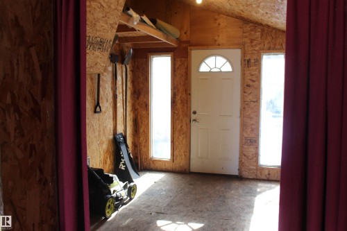 The interior space features wood paneling, a white entry door with an arched window, and two tall windows providing natural light - Edmonton, AB - Indoor Photo Showing Other Room