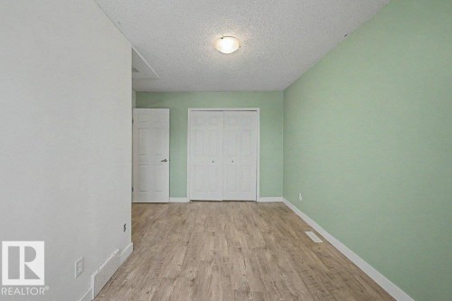 This room features light green walls, wood-style flooring, a white door, and a closet with white bi-fold doors - Edmonton, AB - Indoor Photo Showing Other Room