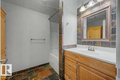 This bathroom features a natural wood vanity with a white countertop and an integrated sink, complemented by a tiled backsplash and mirror - Edmonton, AB - Indoor Photo Showing Bathroom