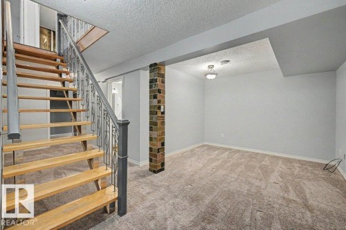 Spacious room featuring light-colored carpet, a ceiling light fixture, and a decorative brick column - Edmonton, AB - Indoor Photo Showing Other Room