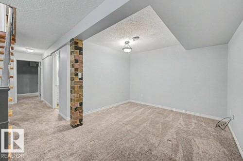 Inviting space featuring light-colored carpeting, white walls, and a decorative brick column - Edmonton, AB - Indoor Photo Showing Other Room