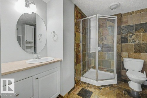 The bathroom features a corner shower with a glass enclosure, a vanity with an oval mirror, and a toilet - Edmonton, AB - Indoor Photo Showing Bathroom