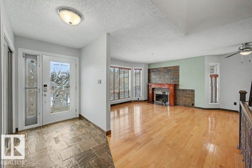 Inviting entry with stone tile flooring leading to a living area featuring hardwood floors, a stone accent wall, and a fireplace with a wood mantel - Edmonton, AB - Indoor With Fireplace