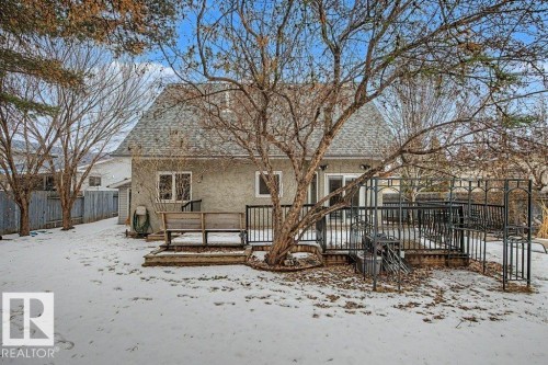 The property features a spacious backyard with a deck and a black metal fence, complemented by mature trees and a shingled roof - Edmonton, AB - Outdoor With Deck Patio Veranda