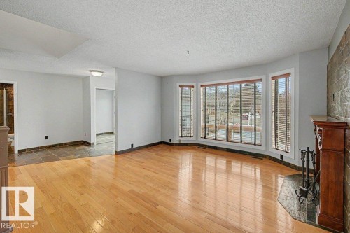 Living area featuring hardwood flooring, a fireplace with a stone surround and wood mantel, and large windows with blinds - Edmonton, AB - Indoor Photo Showing Other Room