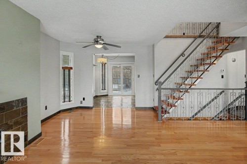 The interior features hardwood flooring, a ceiling fan, and a staircase with a decorative metal railing - Edmonton, AB - Indoor Photo Showing Other Room