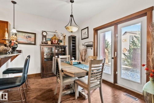 Dining area featuring wood-finish flooring, a pendant light fixture, and double glass-paneled doors with wood trim - 2201 Graybriar Green, Stony Plain, AB - Indoor Photo Showing Dining Room