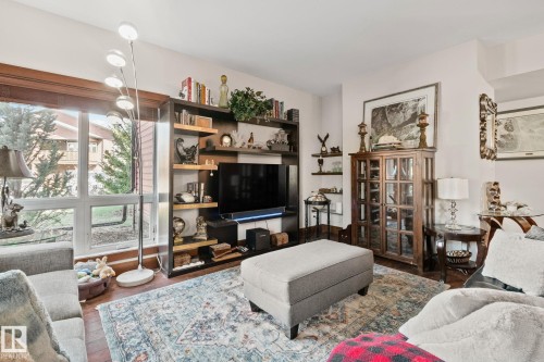 Living area featuring a floor-to-ceiling built-in shelving unit, expansive windows with wood-finish trim, recessed wall shelving, and wood-finish flooring - 2201 Graybriar Green, Stony Plain, AB - Indoor Photo Showing Living Room