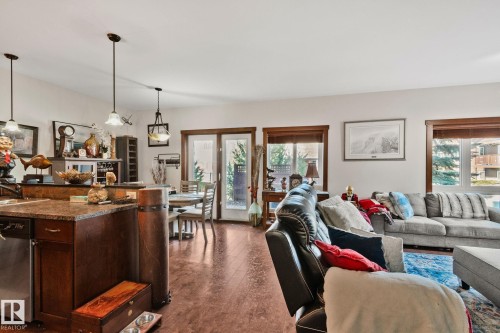 Open-concept living space featuring wood-finish flooring, a kitchen island with stone countertop, pendant lighting, and multiple windows with wood trim - 2201 Graybriar Green, Stony Plain, AB - Indoor Photo Showing Living Room