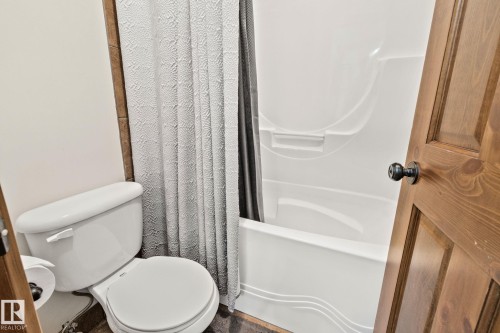 Bathroom featuring a white toilet, a shower/tub combination with a white surround, and a wood-paneled door - 2201 Graybriar Green, Stony Plain, AB - Indoor Photo Showing Bathroom