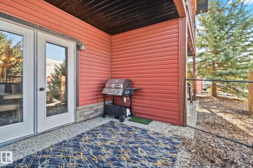 Ground-level patio featuring double glass panel doors, red siding, and a stone base - 2201 Graybriar Green, Stony Plain, AB - Outdoor With Deck Patio Veranda With Exterior