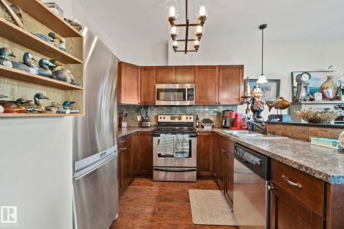 U-shaped kitchen featuring wood-finish cabinetry, stainless steel appliances, a tile backsplash, and composite countertops - 2201 Graybriar Green, Stony Plain, AB - Indoor Photo Showing Kitchen
