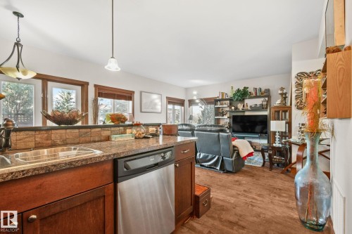 Kitchen featuring a stainless steel dishwasher, brown wood cabinetry, stone-finish countertops, and a tile backsplash - 2201 Graybriar Green, Stony Plain, AB - Indoor Photo Showing Kitchen With Double Sink