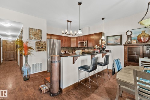 Kitchen and dining area featuring warm wood-finish flooring, rich wood cabinetry, stainless steel appliances, and a breakfast bar with pendant lighting - 2201 Graybriar Green, Stony Plain, AB - Indoor