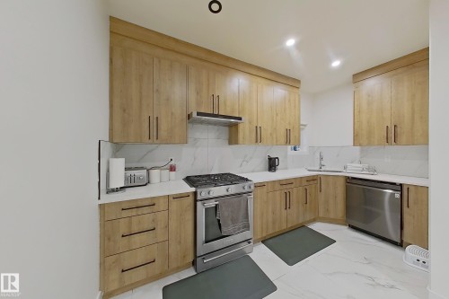 Modern kitchen featuring wood-finish cabinetry, white countertops, a tiled backsplash, stainless steel appliances, and recessed lighting - 1210 Peregrine Terrace, Edmonton, AB - Indoor Photo Showing Kitchen