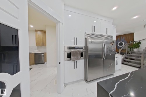 Contemporary kitchen featuring white glossy cabinetry, stainless steel appliances, a built-in oven, recessed lighting, and a dark stone countertop with white veining - 1210 Peregrine Terrace, Edmonton, AB - Indoor