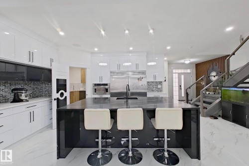 Open-concept kitchen featuring a large central island with seating, stainless steel appliances, white cabinetry with modern hardware, tile backsplash, and recessed lighting - 1210 Peregrine Terrace, Edmonton, AB - Indoor Photo Showing Other Room