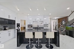 Open-concept kitchen featuring a large central island with seating, stainless steel appliances, white cabinetry with modern hardware, tile backsplash, and recessed lighting - 