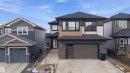 Contemporary two-story residence featuring a dark gray roofline, a mixed-material exterior with tan siding and stone veneer accents, and a dark gray garage door with frosted glass panels - 1210 Peregrine Terrace, Edmonton, AB  - Outdoor With Facade 
