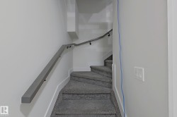 Carpeted staircase with contemporary grey wall-mounted handrail, recessed wall lighting, and white baseboards - 