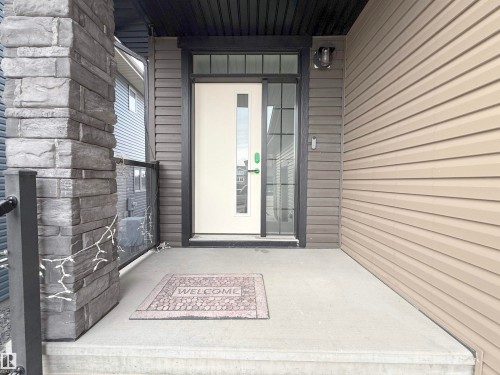 Entryway featuring a stone-clad pillar, concrete porch, and a white door with vertical window panels - 1210 Peregrine Terrace, Edmonton, AB - Outdoor With Exterior