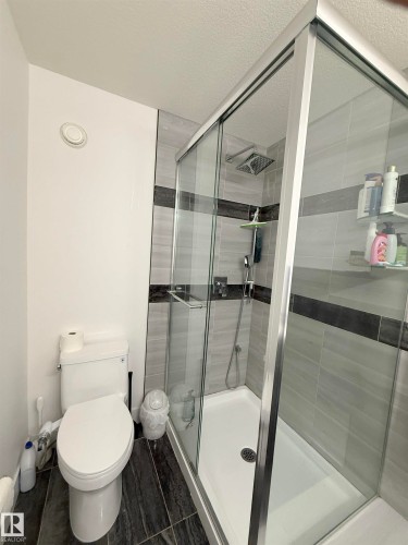 Glass-enclosed shower with a rainfall shower head, handheld shower fixture, and light-toned tile surround with a dark accent band - 1210 Peregrine Terrace, Edmonton, AB - Indoor Photo Showing Bathroom