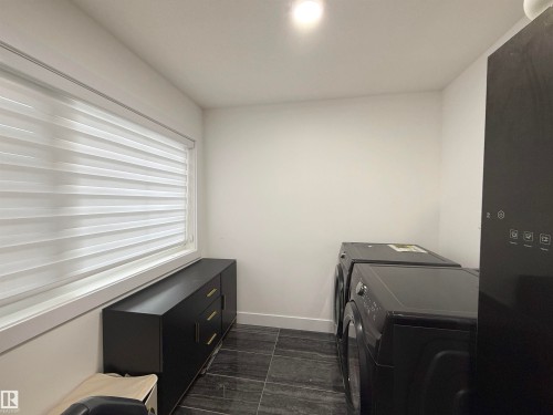 Laundry area featuring dark tile flooring, a horizontal window with blinds, and built-in black cabinetry with gold-tone hardware - 1210 Peregrine Terrace, Edmonton, AB - Indoor Photo Showing Laundry Room