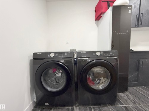 Dedicated laundry area featuring modern front-load appliances, dark wood-finish flooring, white walls, and built-in cabinetry with a light countertop - 1210 Peregrine Terrace, Edmonton, AB - Indoor Photo Showing Laundry Room