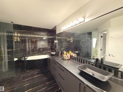 Bathroom featuring full-height black and gold veined tile, a freestanding soaking tub, and a glass-enclosed shower - 